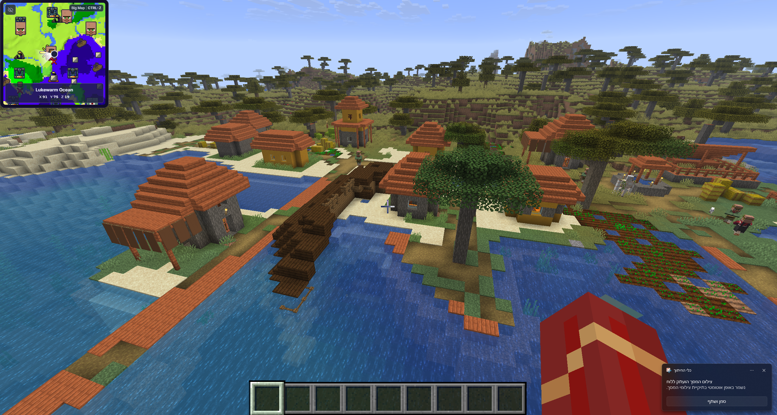 Minecraft gameplay overlooking a waterside savanna village with the MineyMap minimap visible